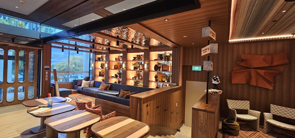Site progress photograph of the QT arrival spaces, showing illuminated display shelving, ceiling lighting and timber finishes. Small work materials remain visible.